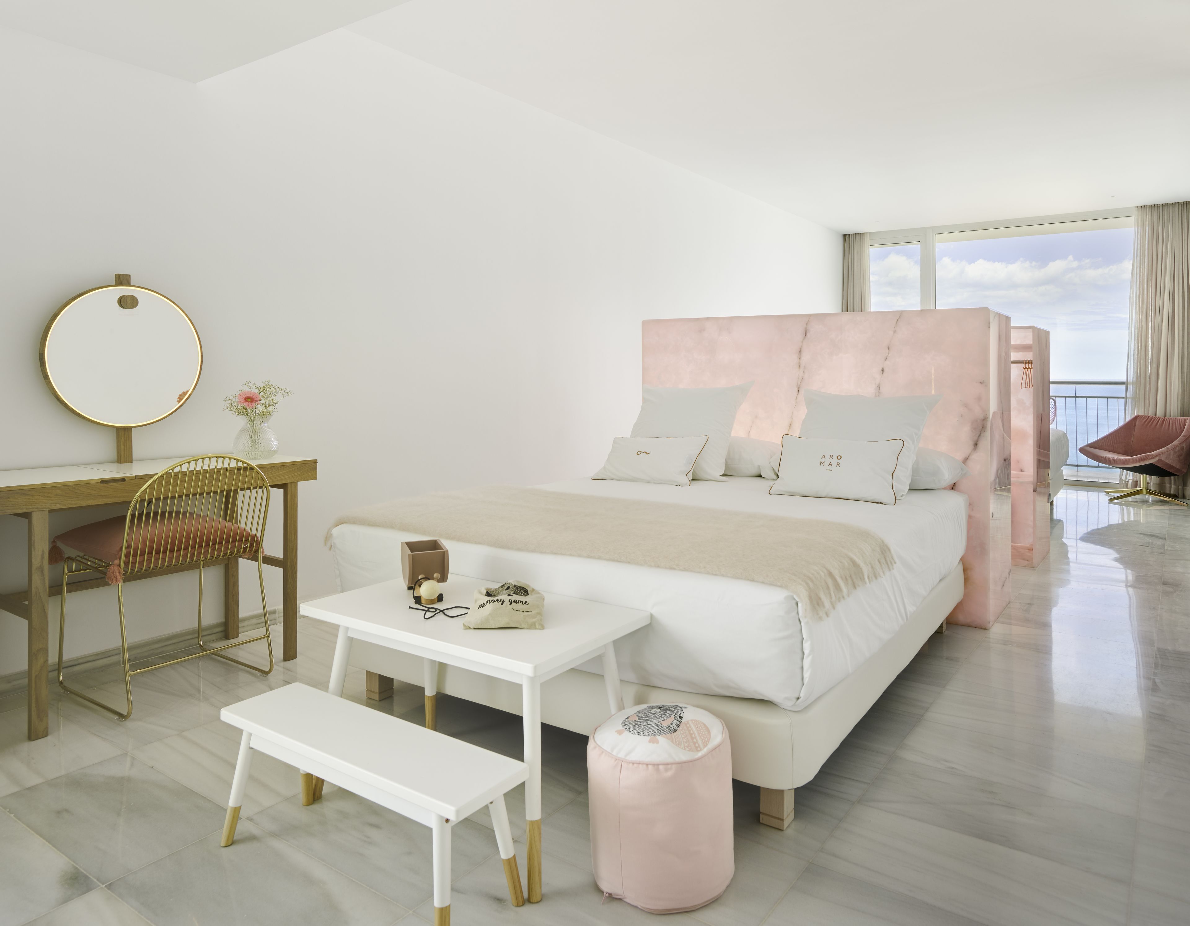 A modern bedroom with a large bed, a bedside table, a chair, a desk, and a window with a view.