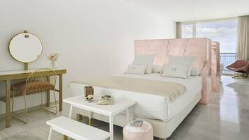 A modern bedroom with a large bed, a bedside table, a chair, a desk, and a window with a view.