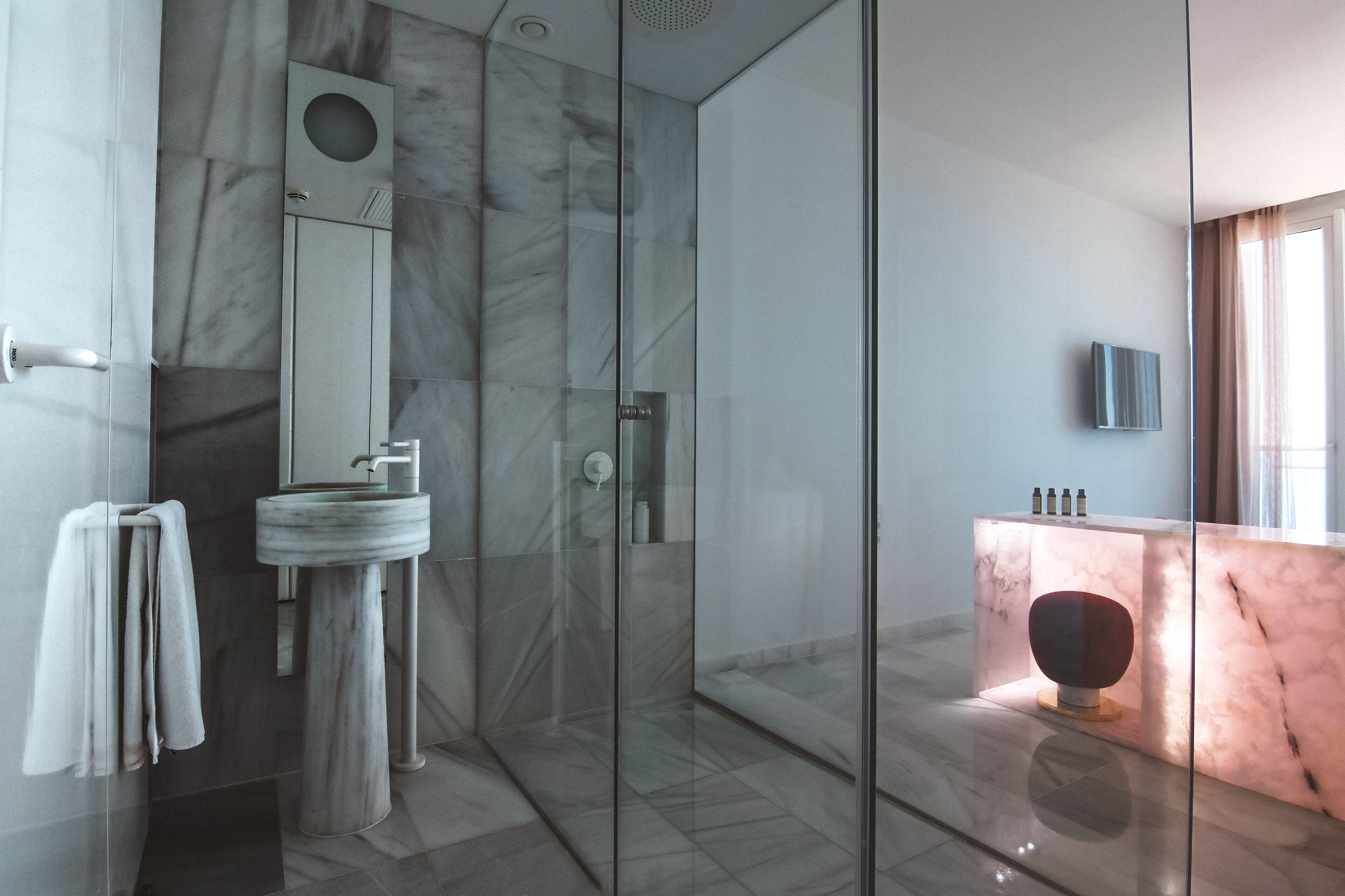 Un baño moderno con lavamanos de mármol, cabina de ducha de vidrio y tocador de mármol.