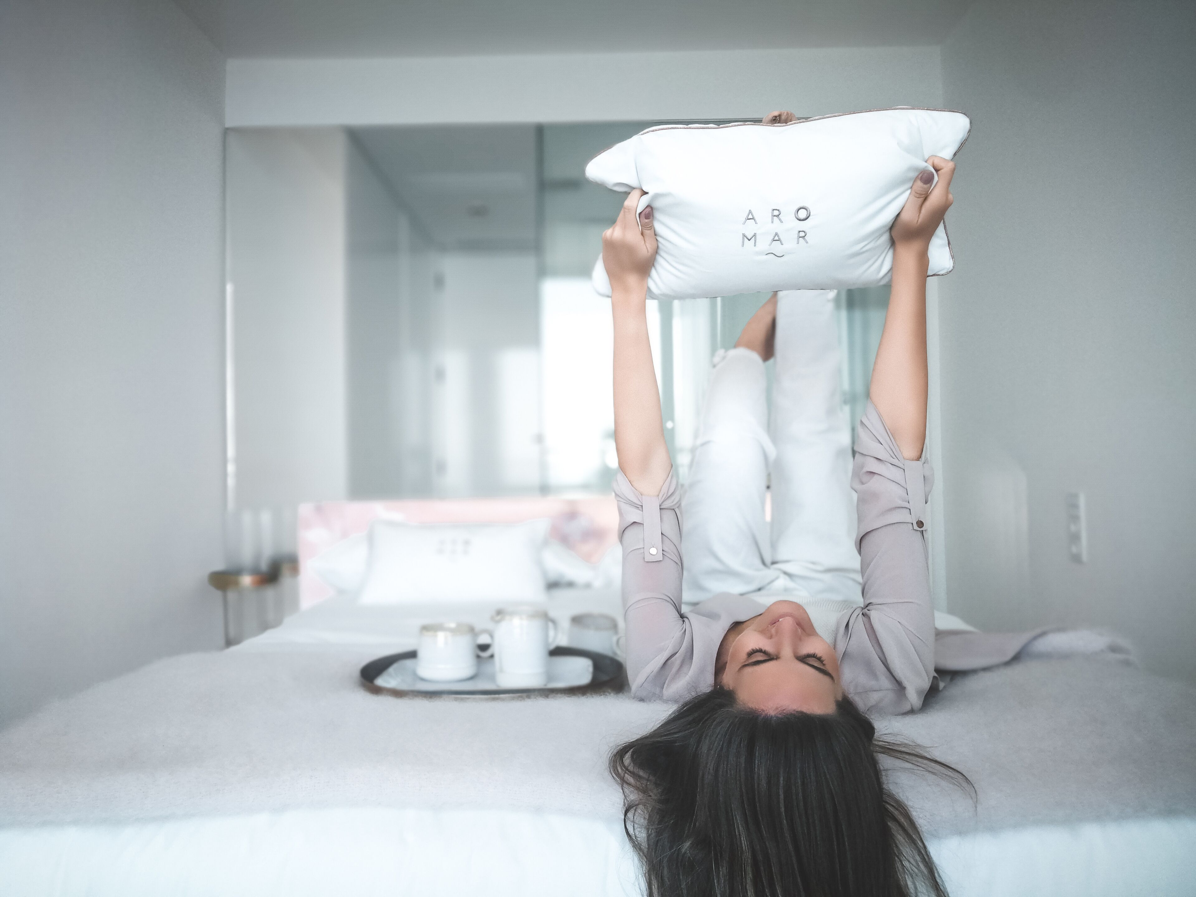 A person lying on a bed with a pillow labeled "ARO MAR" and a tray with two cups.