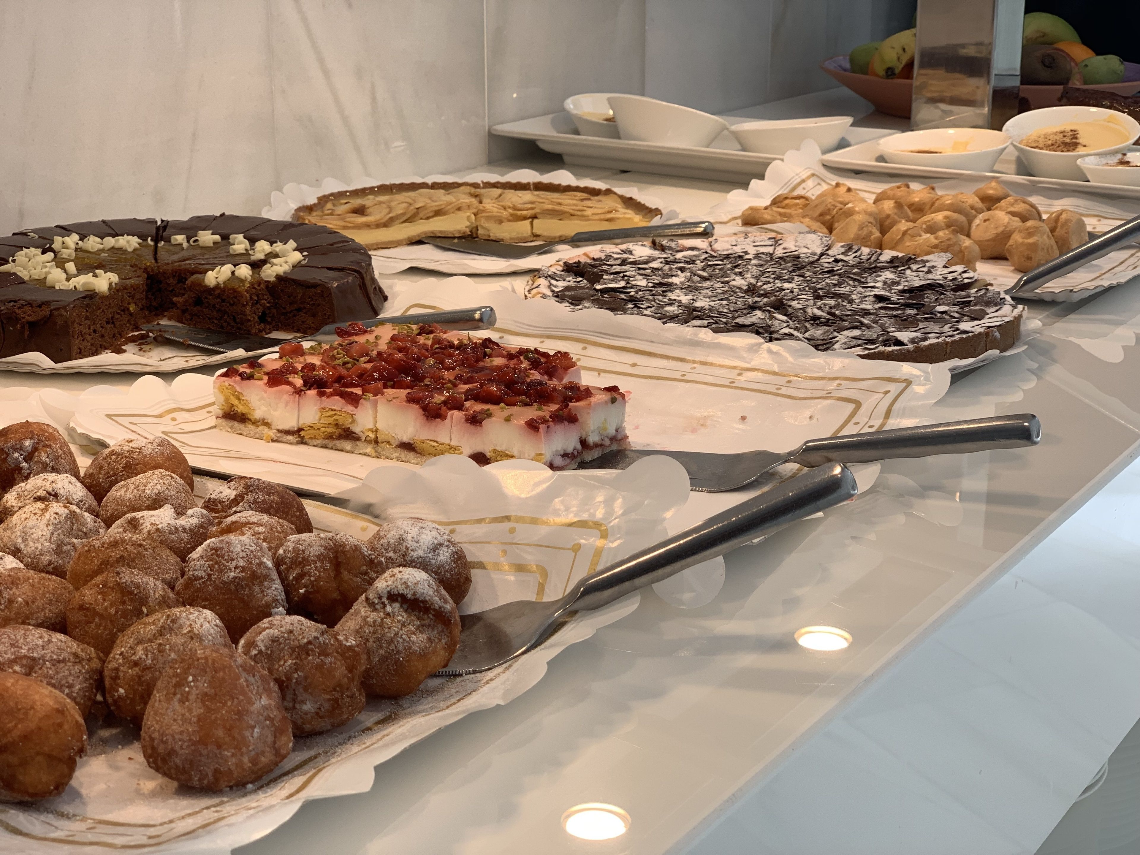 Una variedad de postres, incluyendo pasteles, bollos y una tarta, expuestos en una mesa con utensilios para servir.