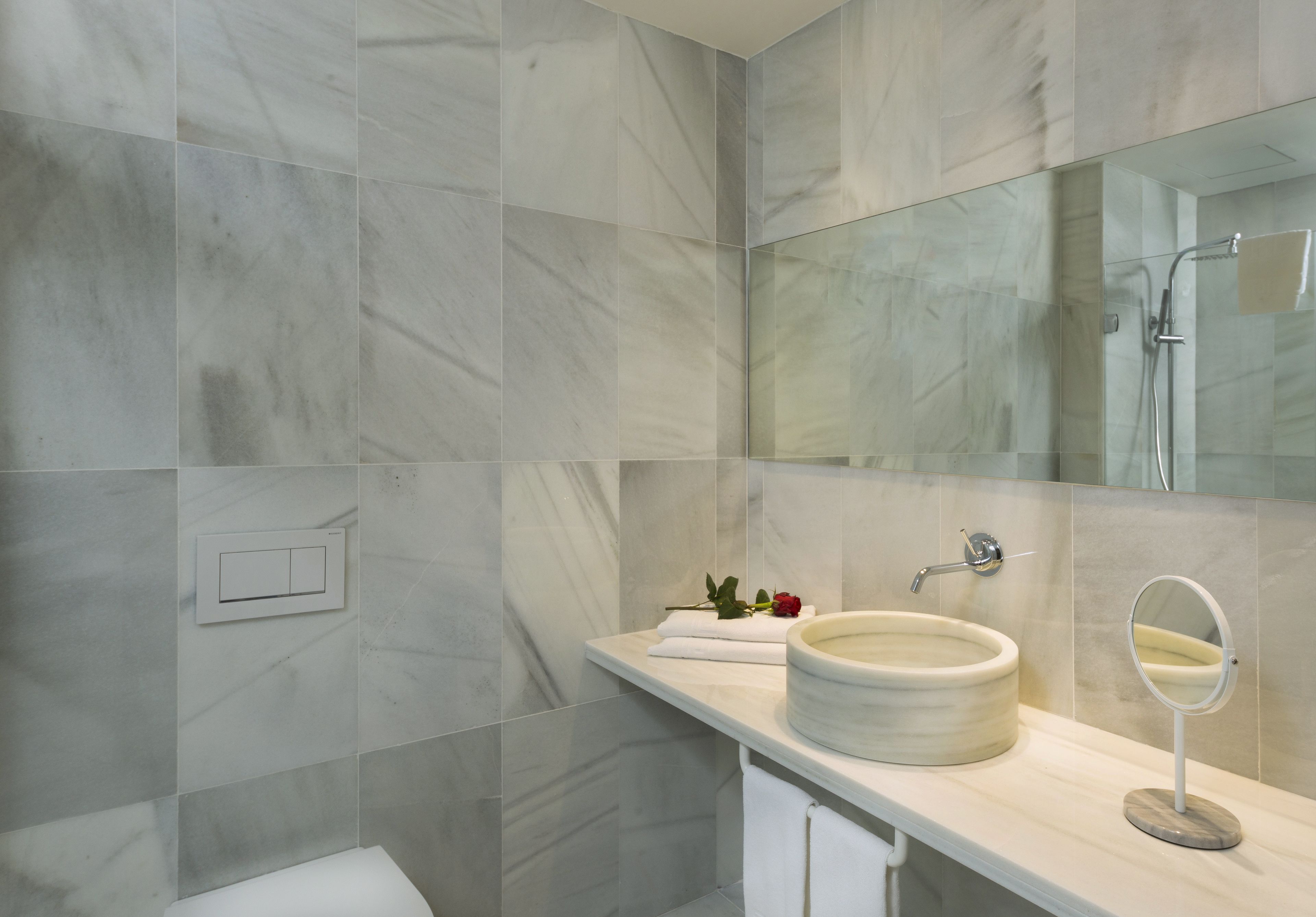 Een moderne badkamer met een marmeren wastafel, een spiegel en een douche.