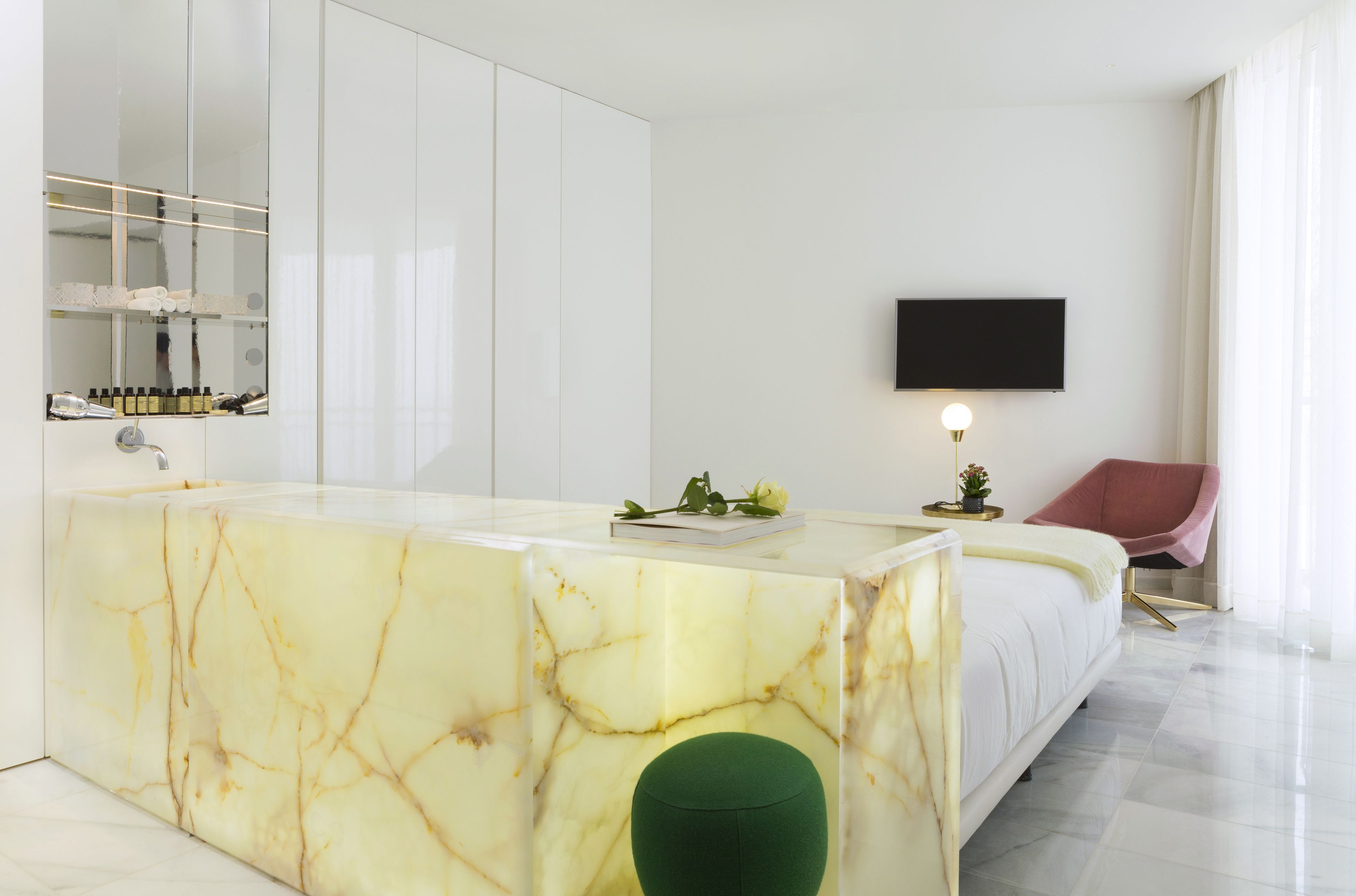 Un dormitorio moderno con tocador de mármol, televisor de pantalla plana y un reposapiés verde.