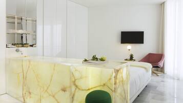 Un dormitorio moderno con tocador de mármol, televisor de pantalla plana y un reposapiés verde.