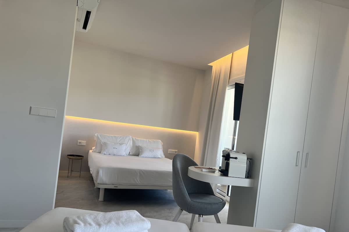Ein modernes Hotelzimmer mit einem ordentlich bezogenen Bett, einem kleinen runden Tisch mit einem Stuhl und einem Schreibtisch mit einem Computer.