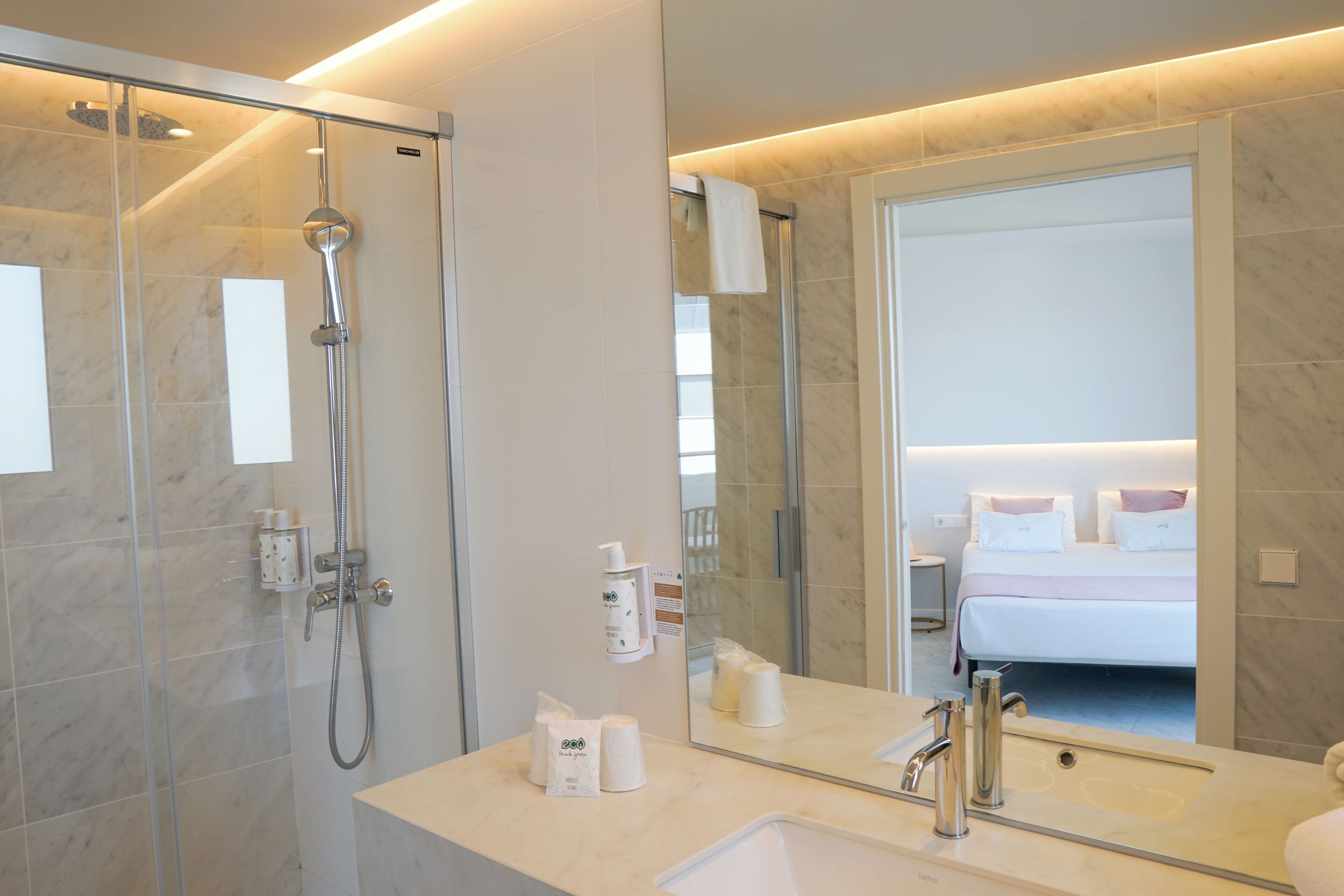 A modern bathroom with a glass-enclosed shower, a large mirror, and a sink with toiletries.