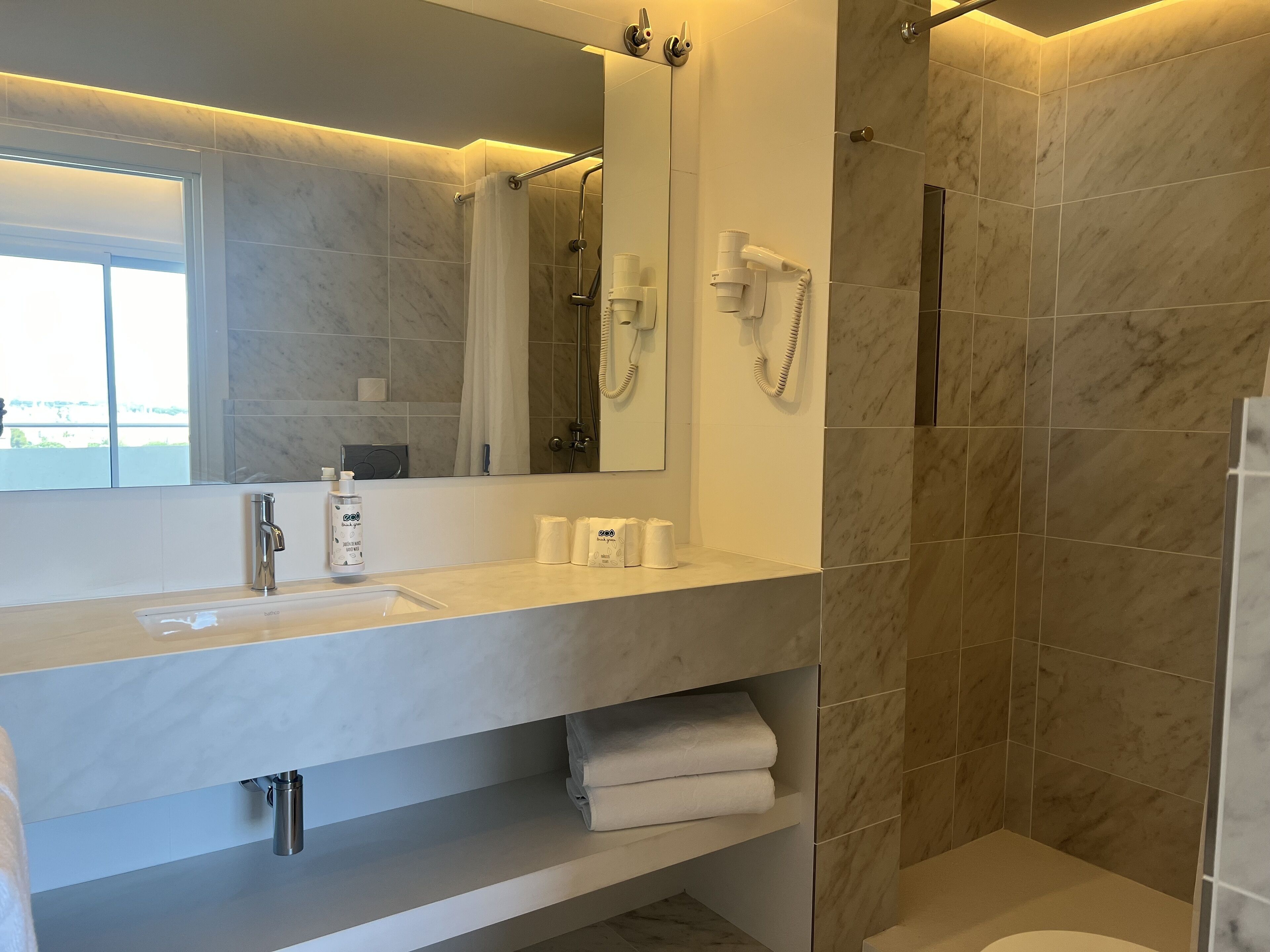 Un baño moderno con un espejo grande, un lavabo, una ducha y un perchero para toallas.