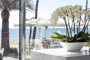 A beachside café with outdoor seating, a white orchid in a pot, and a view of the sea. - Hotel Aromar (Castell-Platja d'Aro)