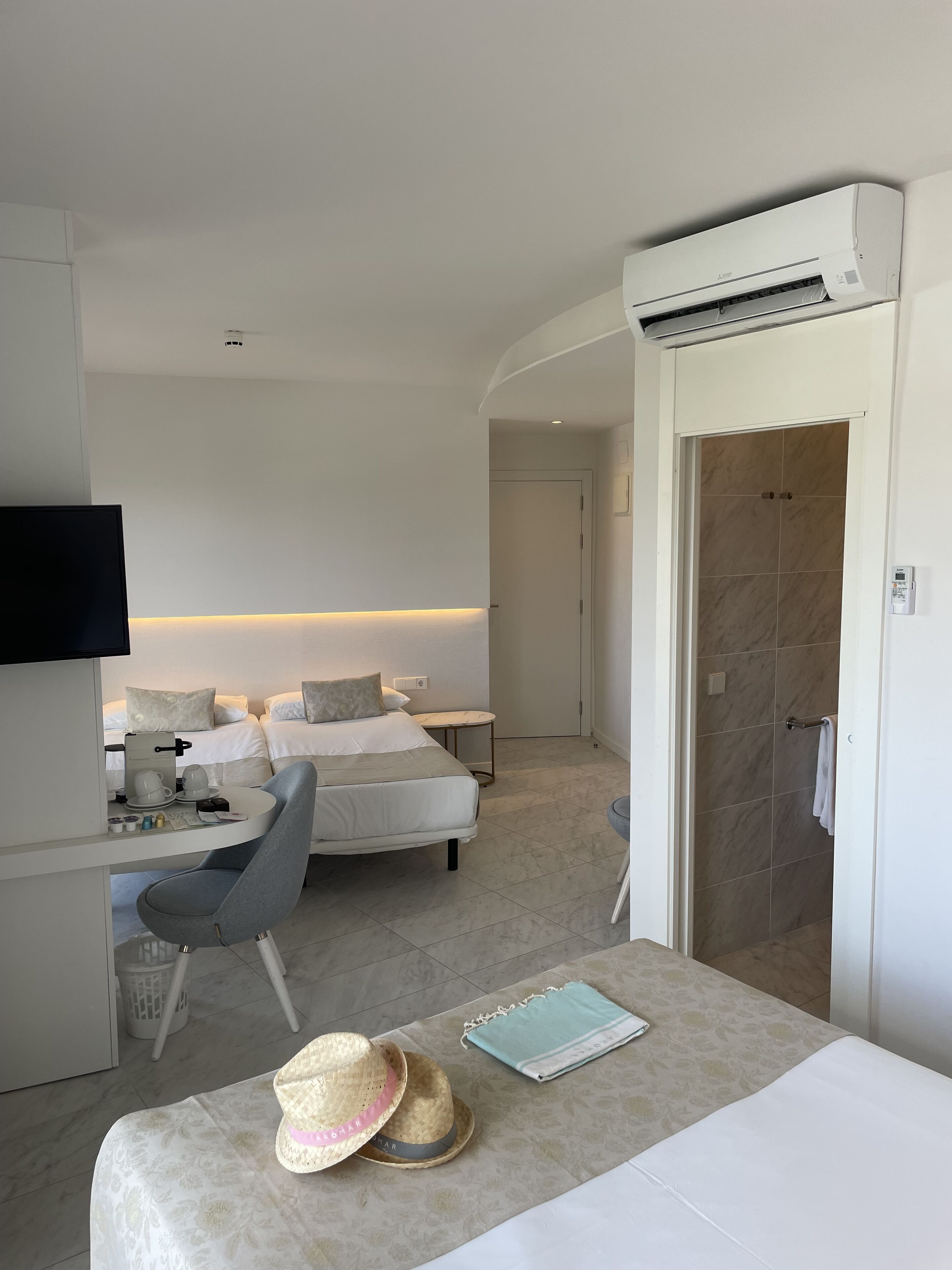 A hotel room with a bed, a desk with a chair, a TV, and an air conditioning unit.