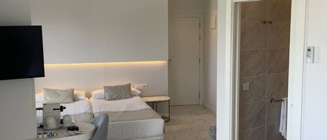 A hotel room with a bed, a desk with a chair, a TV, and an air conditioning unit.