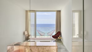 Habitación de hotel moderna con escritorio de mármol, dos sillas y un amplio ventanal con vista al mar.