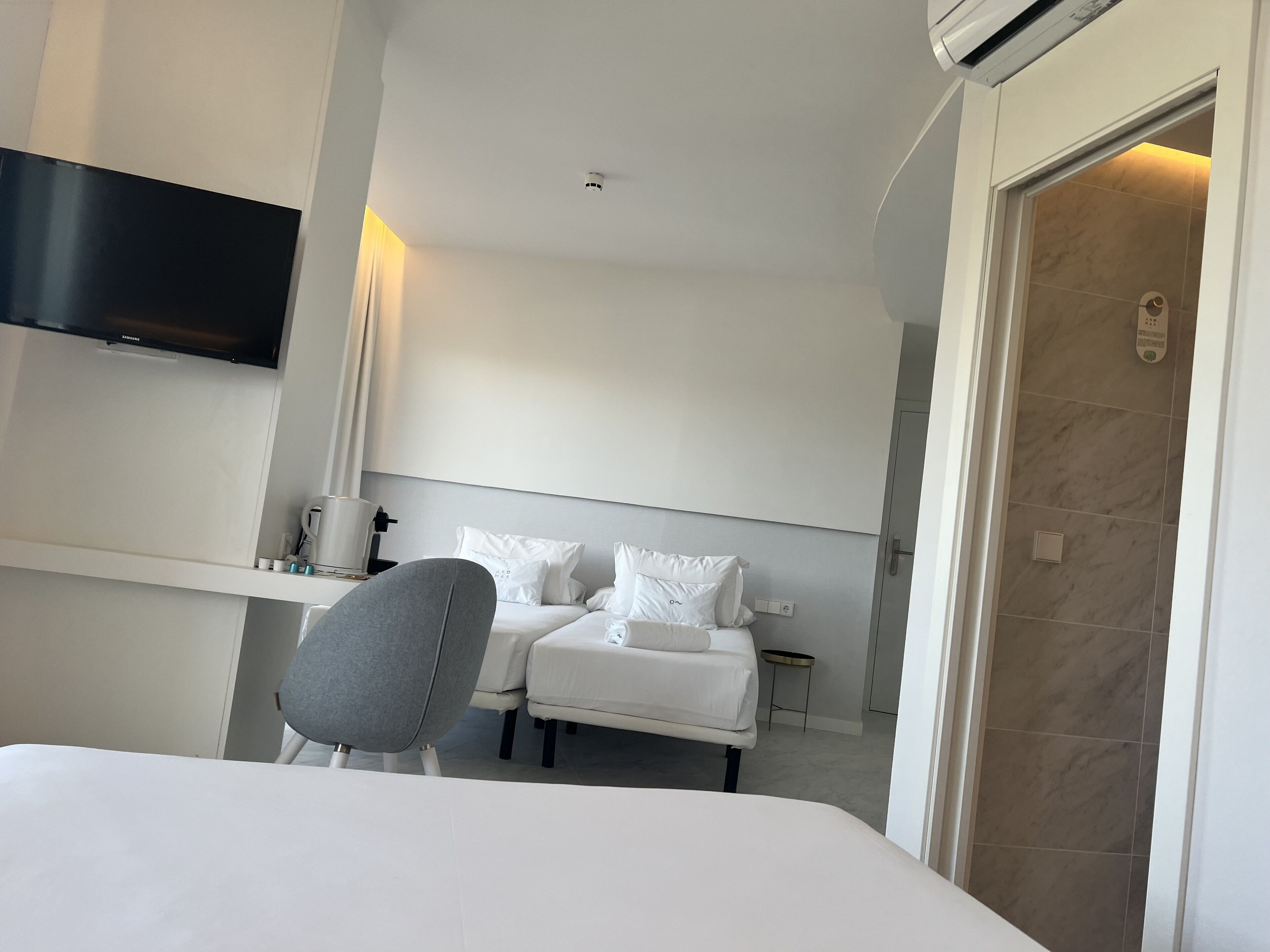 Habitación de hotel con cama, una silla, televisor montado en la pared y zona de ducha.