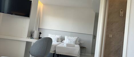 Habitación de hotel con cama, una silla, televisor montado en la pared y zona de ducha.