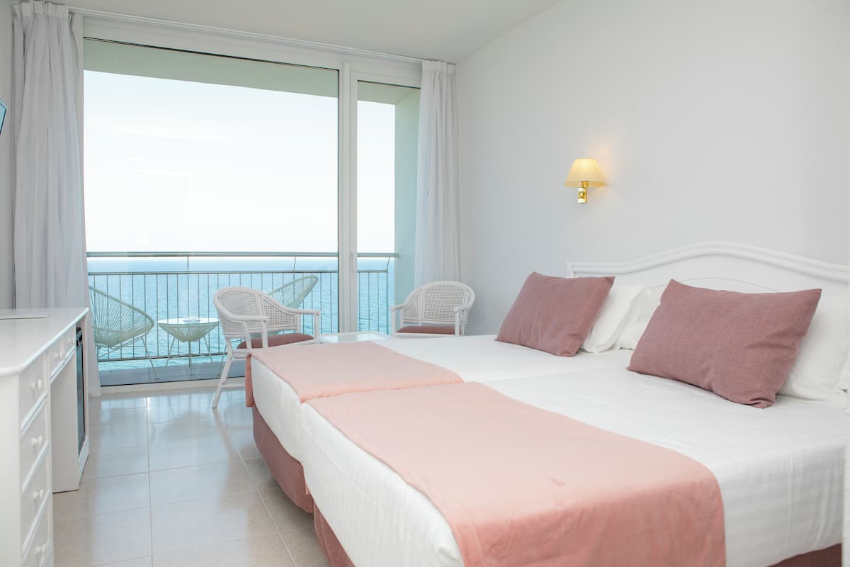 Ein Hotelzimmer mit Balkon, einem Bett mit rosa Bettwäsche, weißen Möbeln und einer wandmontierten Lampe.
