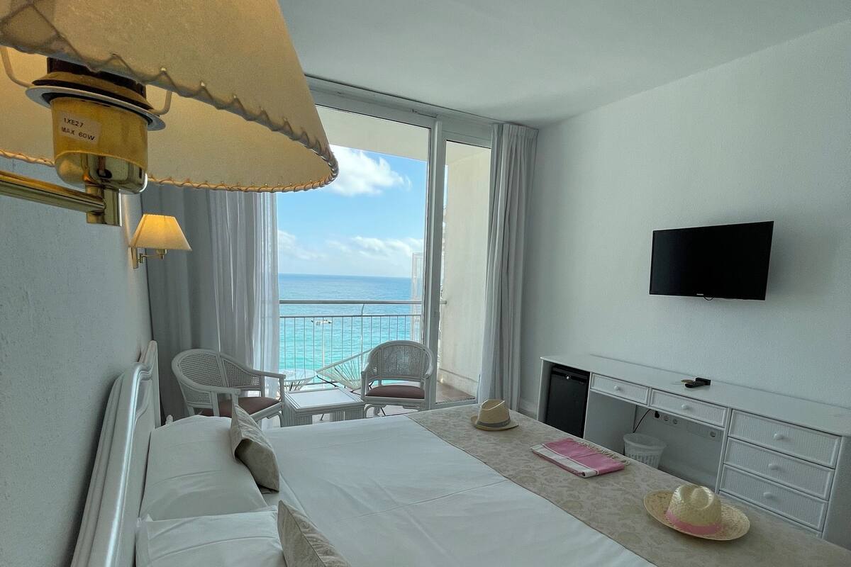 Ein Hotelzimmer mit Bett, Schreibtisch, Stuhl, Fernseher und Meerblick.