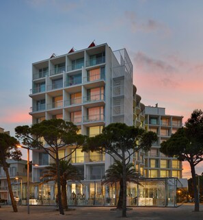 A modern multi-story hotel with balconies, glass storefronts, and a sunset sky. - Hotel Aromar (Castell-Platja d'Aro)