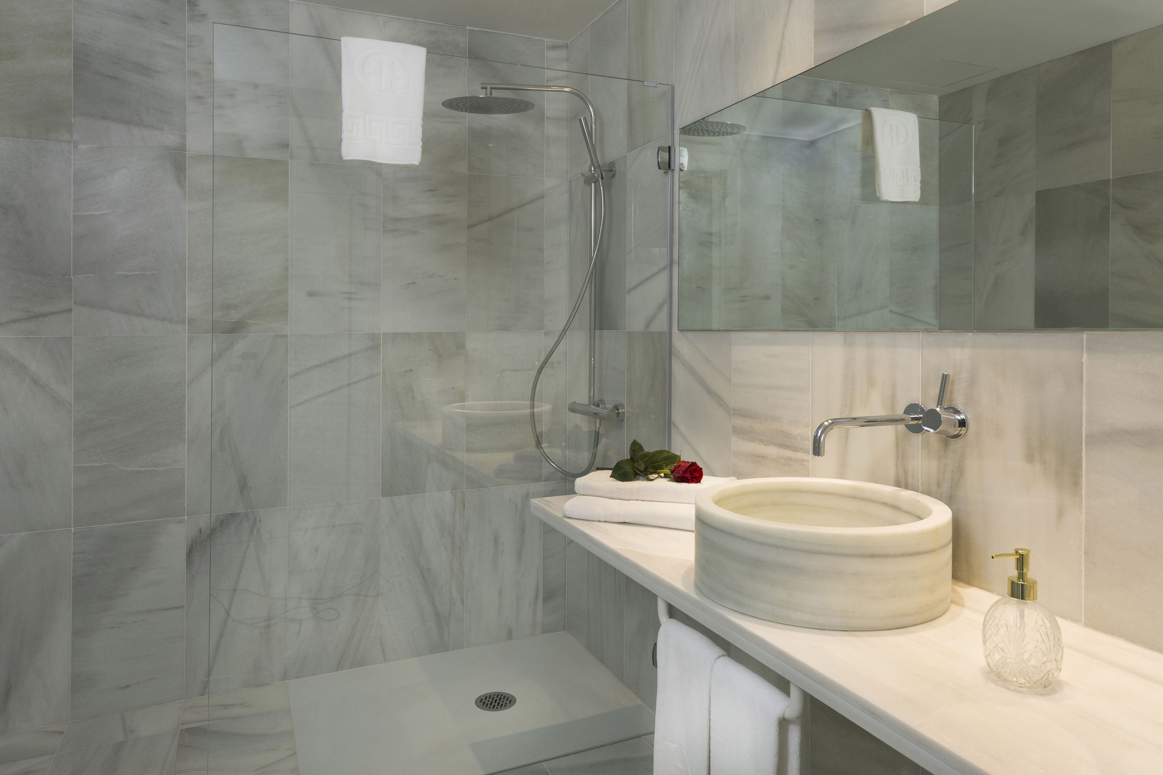 A modern bathroom with a glass-enclosed shower, a marble sink, and a large mirror.