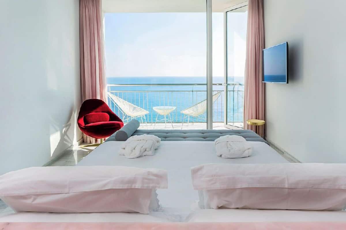 Ein Hotelzimmer mit einem großen Bett, zwei weißen Kissen, einem roten Sessel und einem Fernseher an der Wand.