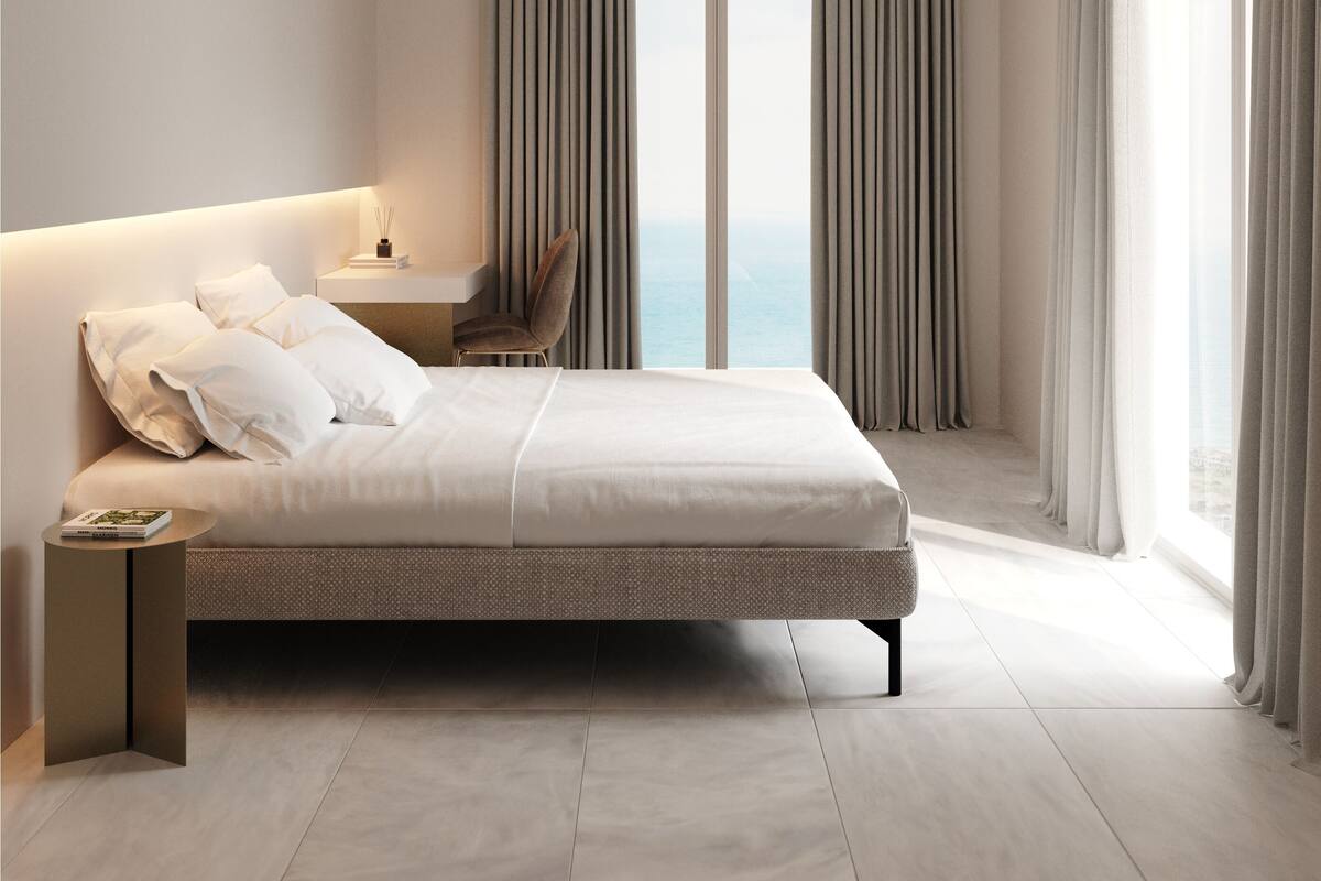 Ein modernes Hotelzimmer mit einem großen Bett, einem Nachttisch, einem Sessel und Meerblick durch raumhohe Fenster.
