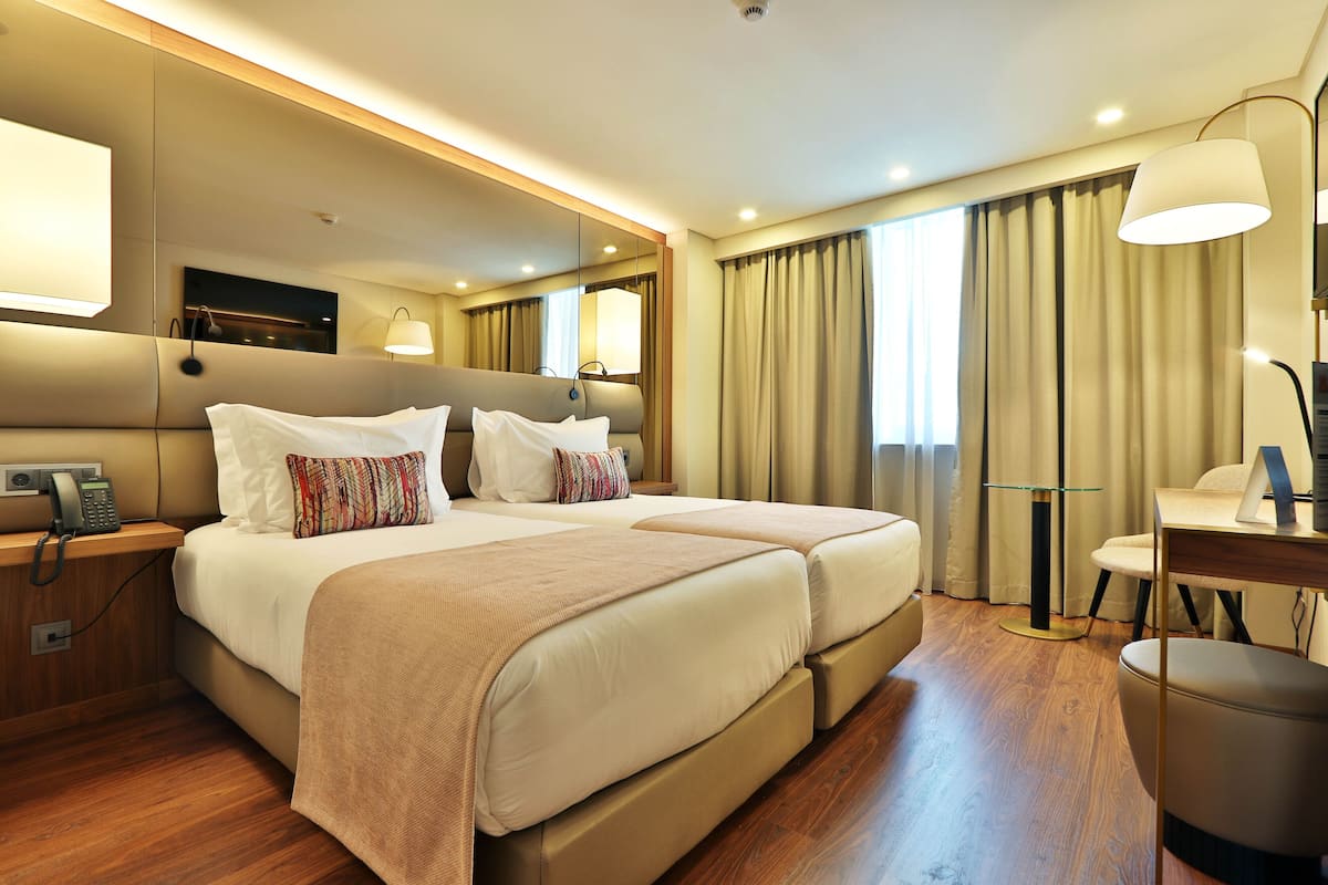 A hotel room with two beds, a desk, a chair, a telephone, and a mirror.