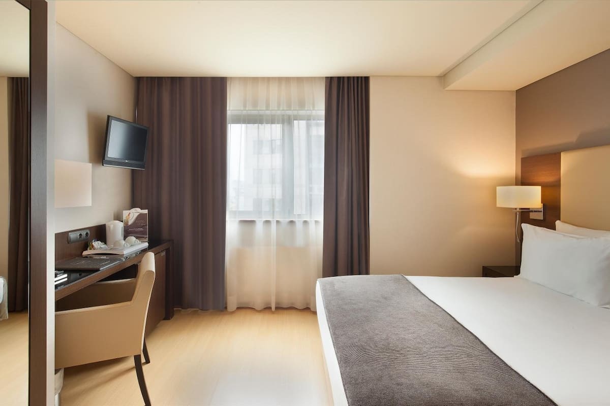 A hotel room with a bed, desk, chair, television, and a window with curtains.