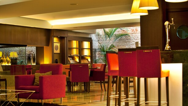 Eine moderne Lobby mit roten Stühlen, einer Bar und einem großen Fenster mit Blick auf Grünflächen.