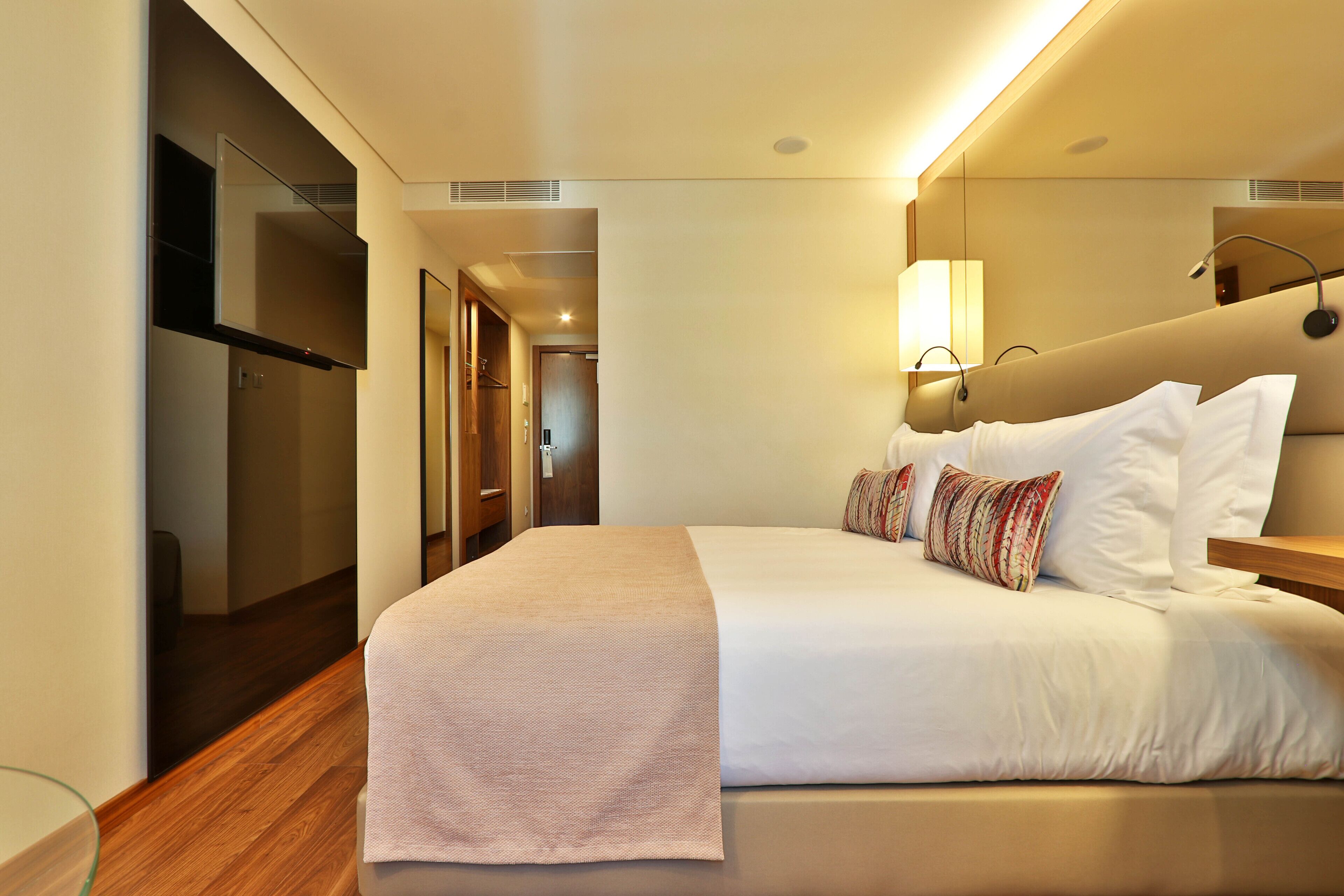 A hotel room with a bed, bedside table, lamp, and a mirror.