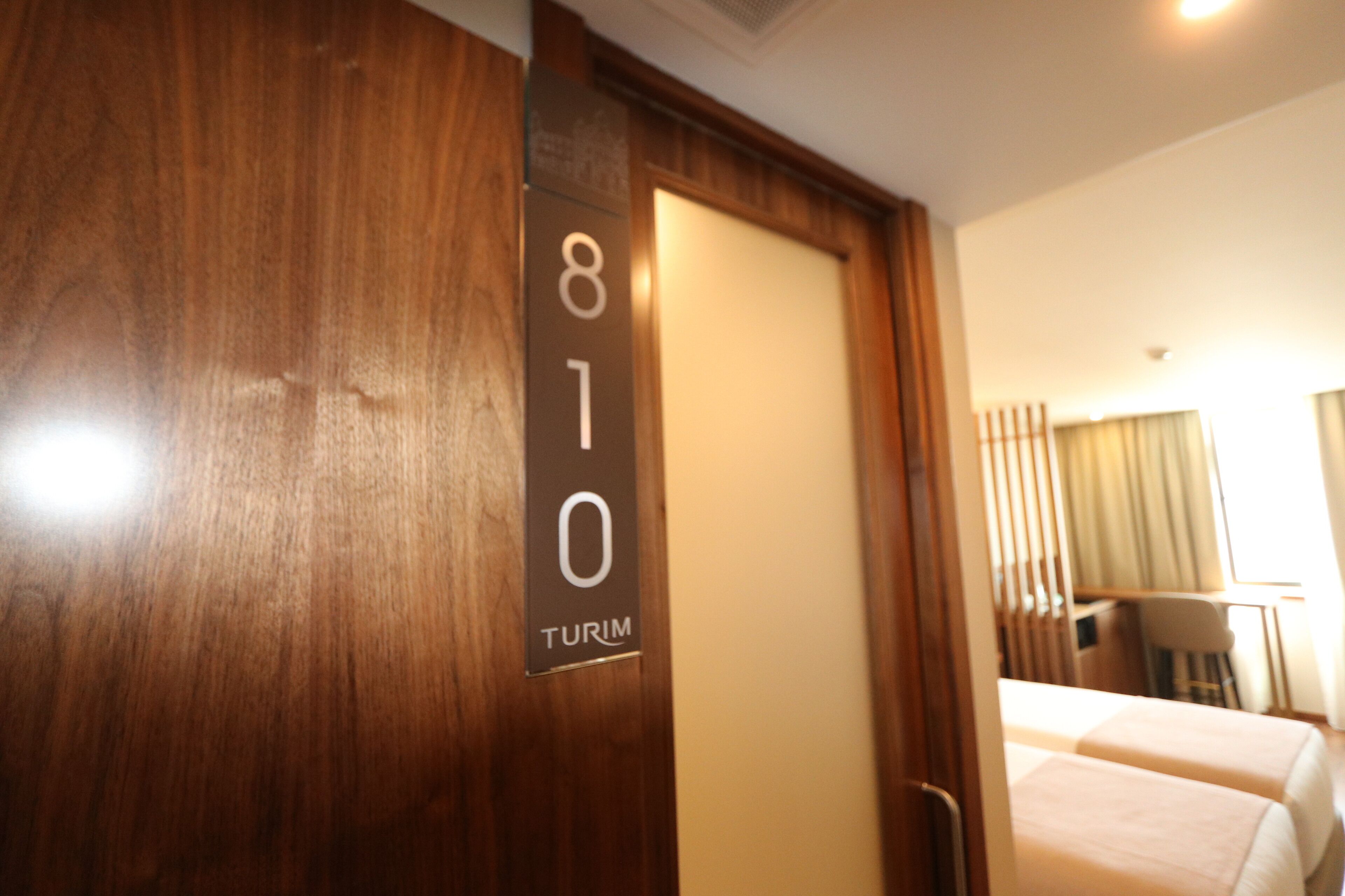 A hotel room with a wooden door marked "810 TURIM" and two beds with white bedding.