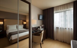A hotel room with a bed, desk, chair, TV, and a window with curtains.