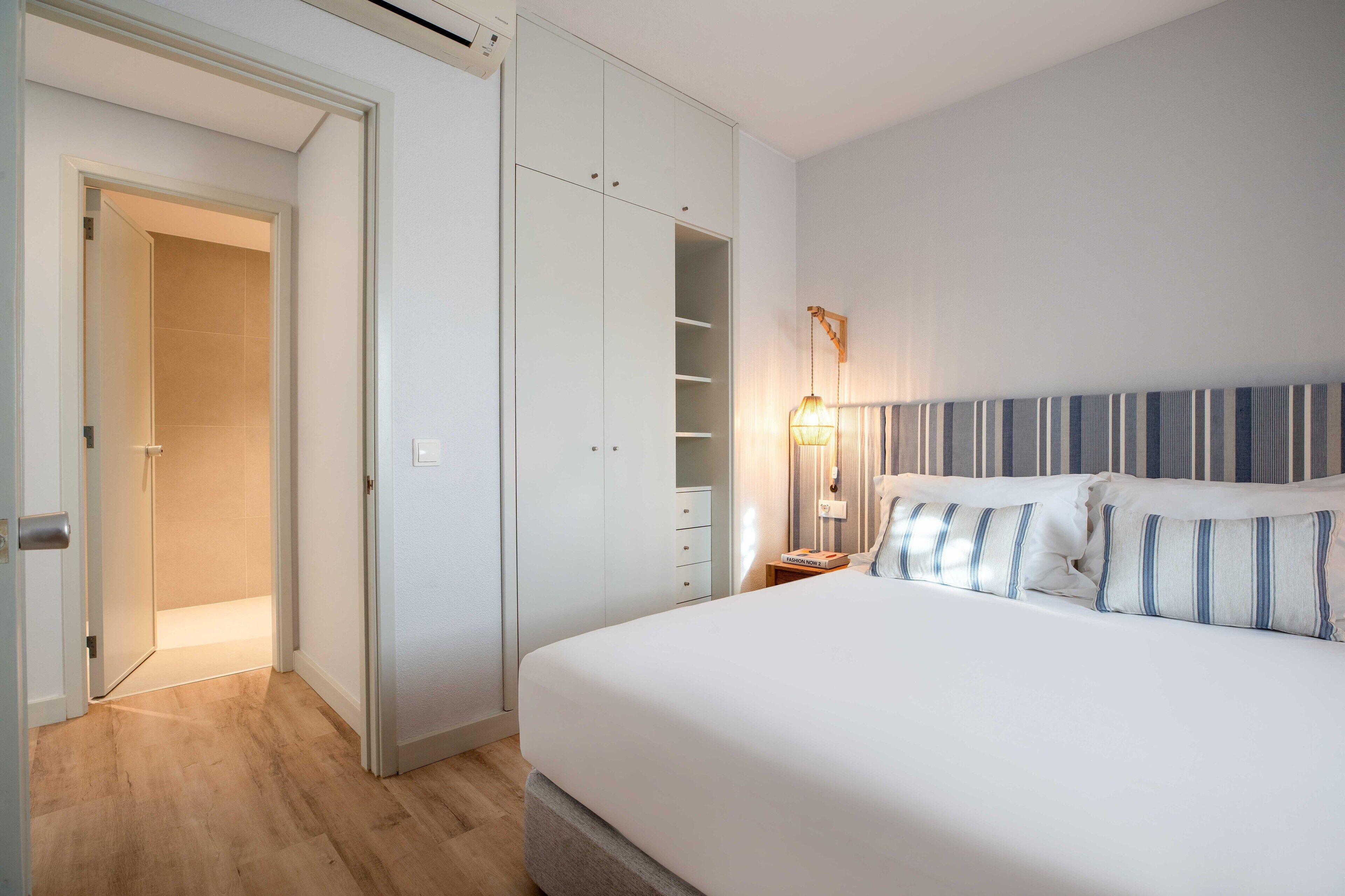 Ein Schlafzimmer mit Bett, Kleiderschrank, Nachttisch und Lampe.
