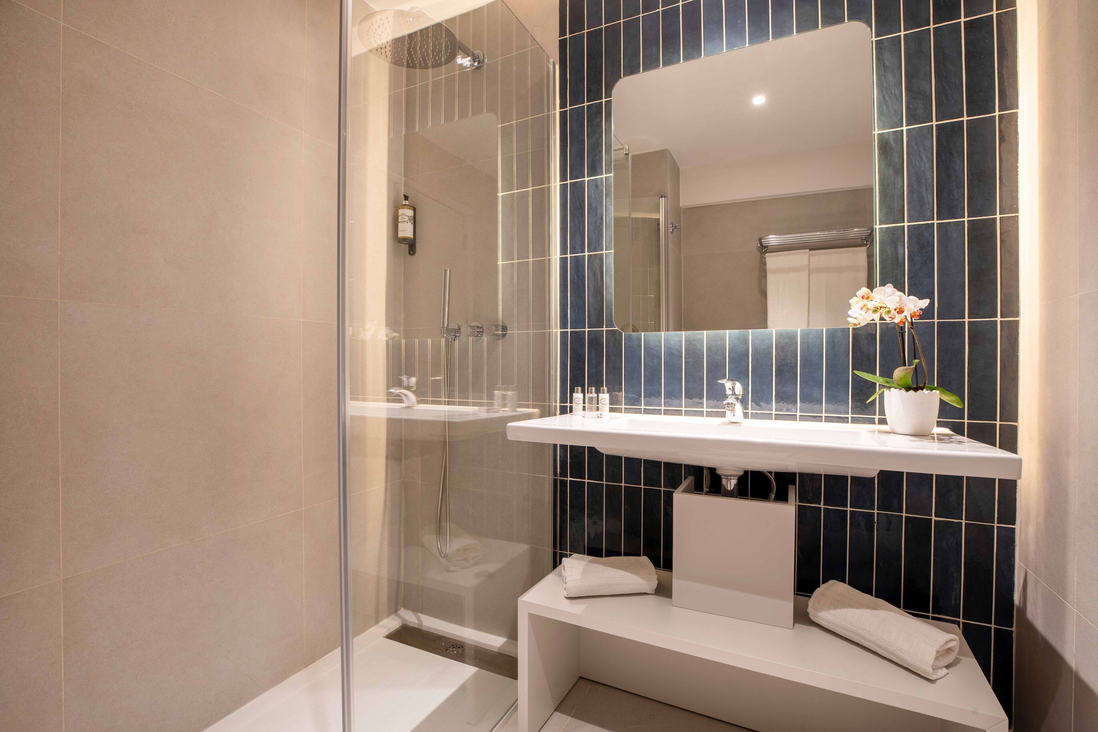 A modern bathroom with a glass-enclosed shower, a white vanity with a mirror, and a bench.