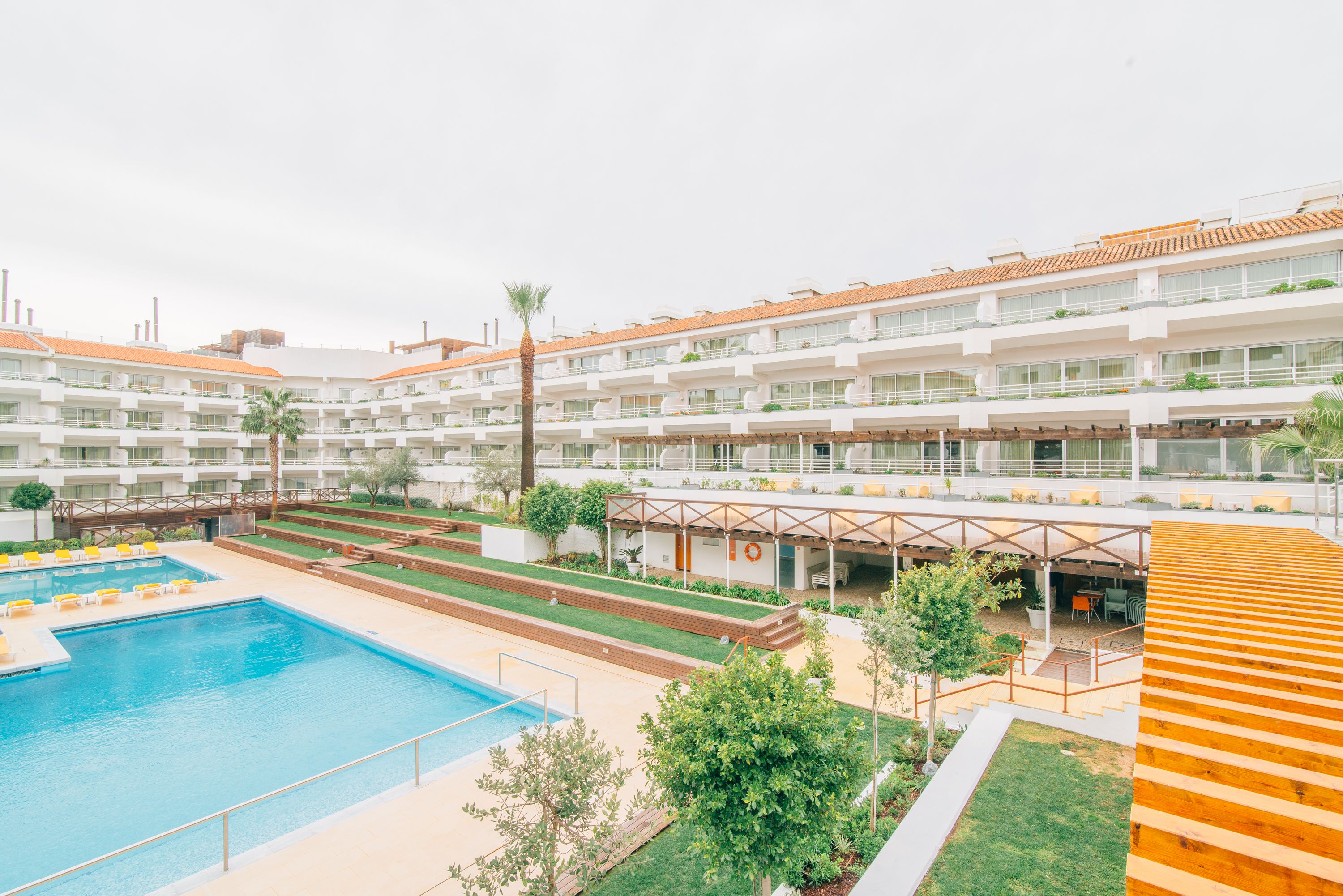 A hotel with multiple balconies, a swimming pool, and a covered outdoor seating area.