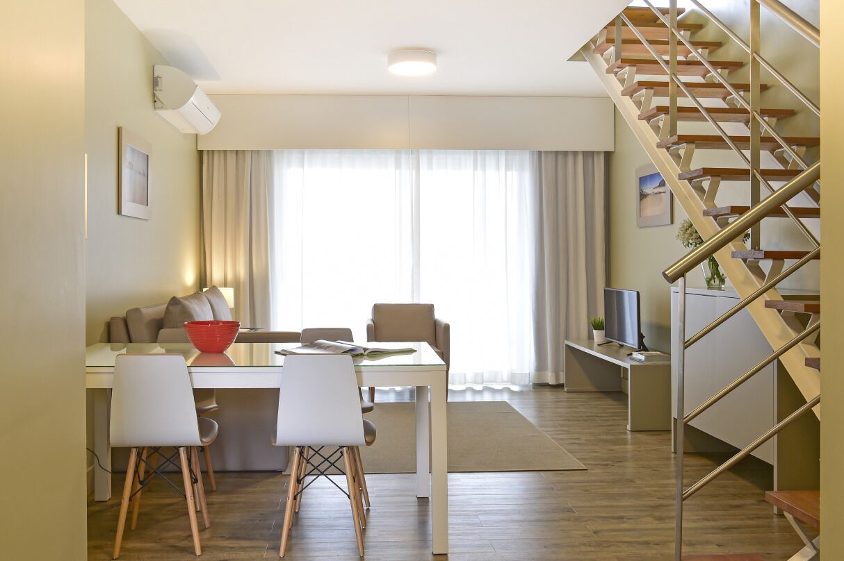Een moderne woonkamer met een eethoek, een trap en een groot raam met gordijnen.