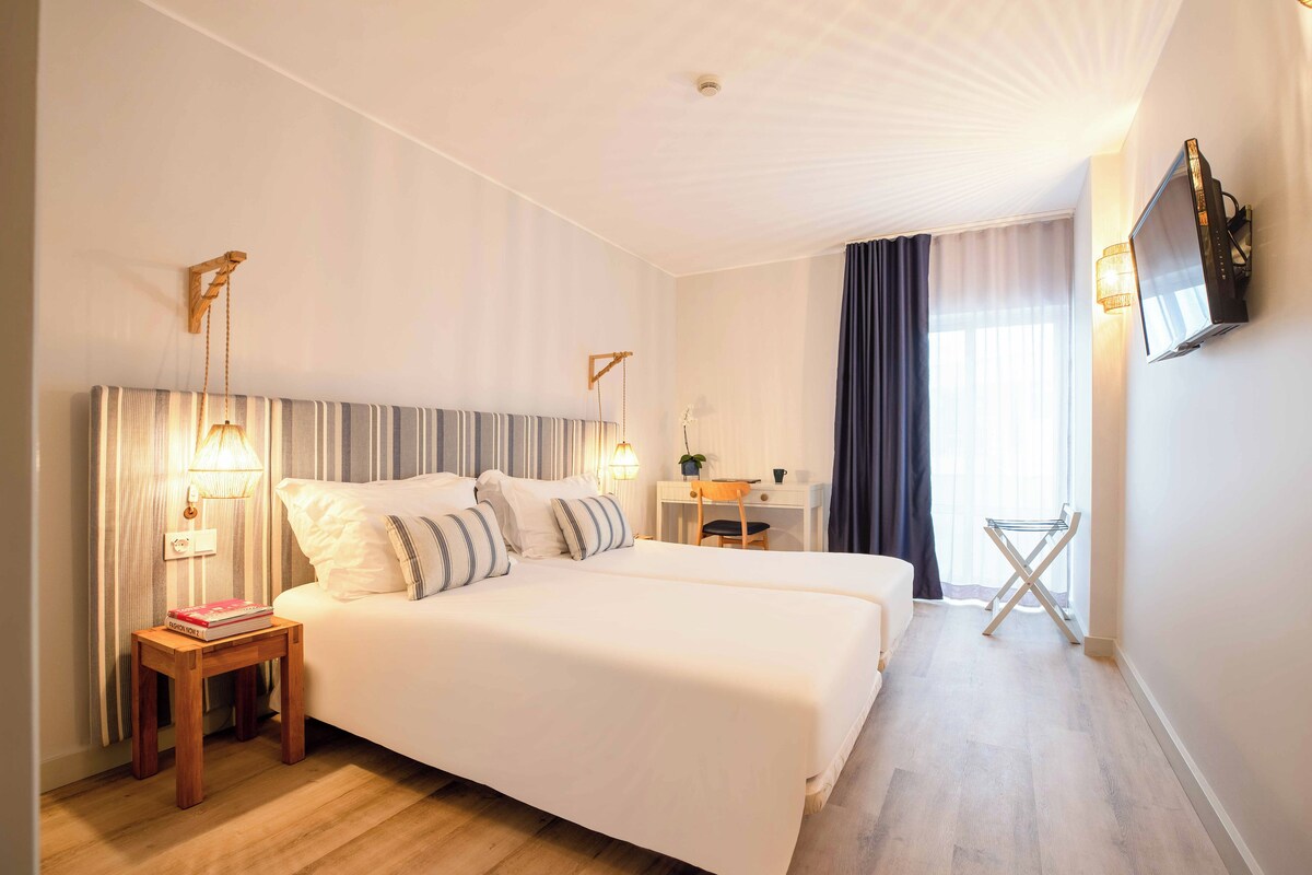 Una habitación de hotel con una cama grande, mesitas de noche, un escritorio, un televisor y una ventana con cortinas.
