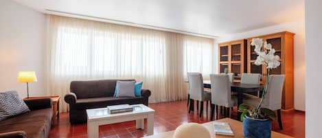A living room with a sofa, coffee table, dining table, chairs, and a potted plant.