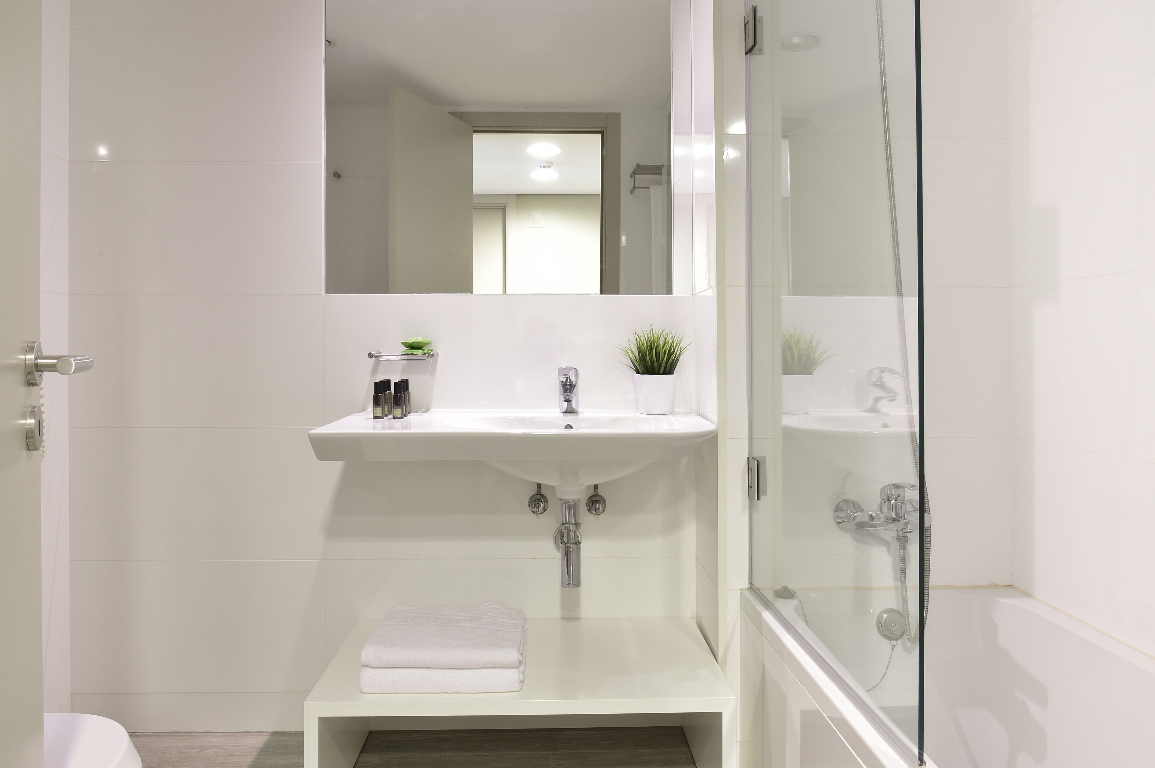 Une salle de bain moderne avec un lavabo blanc, une douche en verre et une petite étagère contenant des articles de toilette.