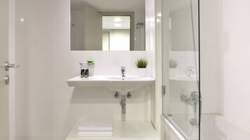 A modern bathroom with a white sink, a glass shower enclosure, and a small shelf with toiletries.
