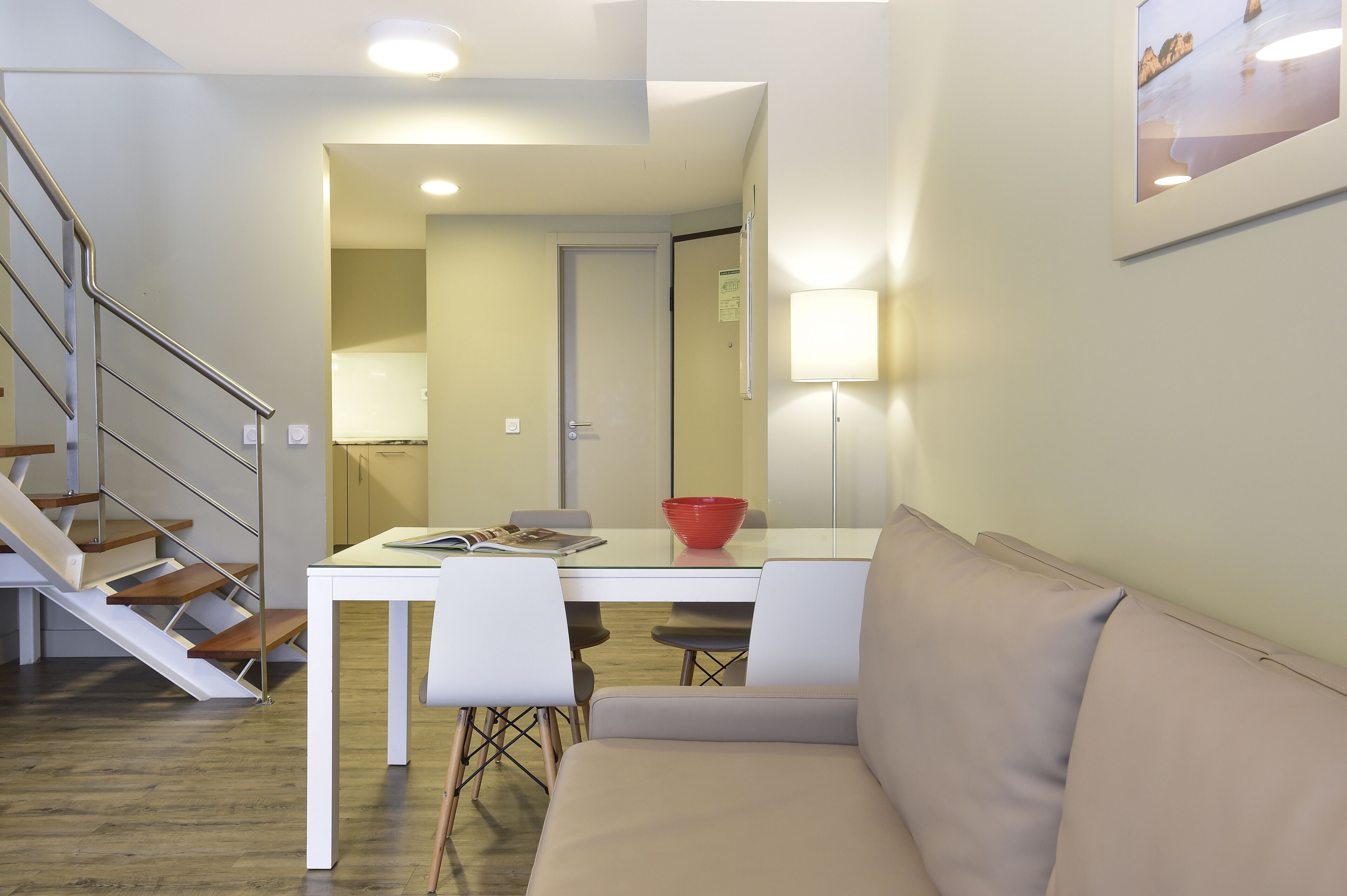 A modern living space with a staircase, a dining area with a table and chairs, a sofa, and a lamp.