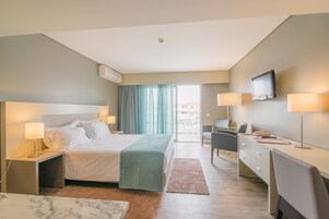 A hotel room with a bed, desk, chair, TV, and a view of the outside.