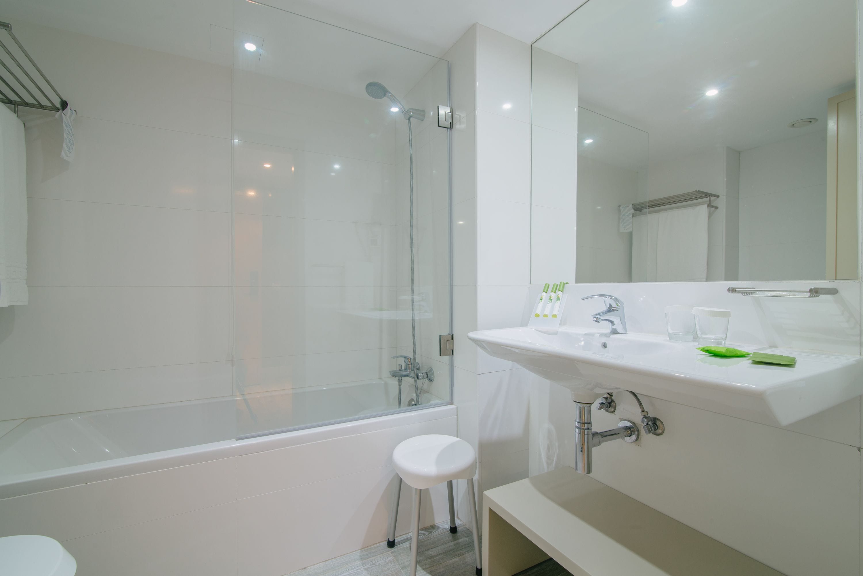 A modern bathroom with a glass-enclosed shower, a white sink with a mirror, and a small stool.
