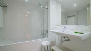 A modern bathroom with a glass-enclosed shower, a white sink with a mirror, and a small stool.