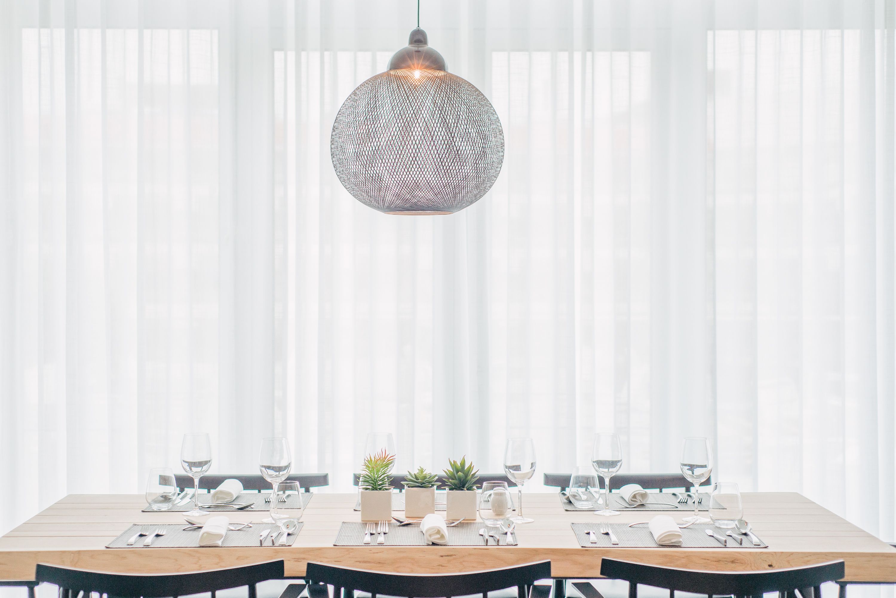 Een eetruimte met een houten tafel voor zes personen, plantenpotten en een hanglamp.