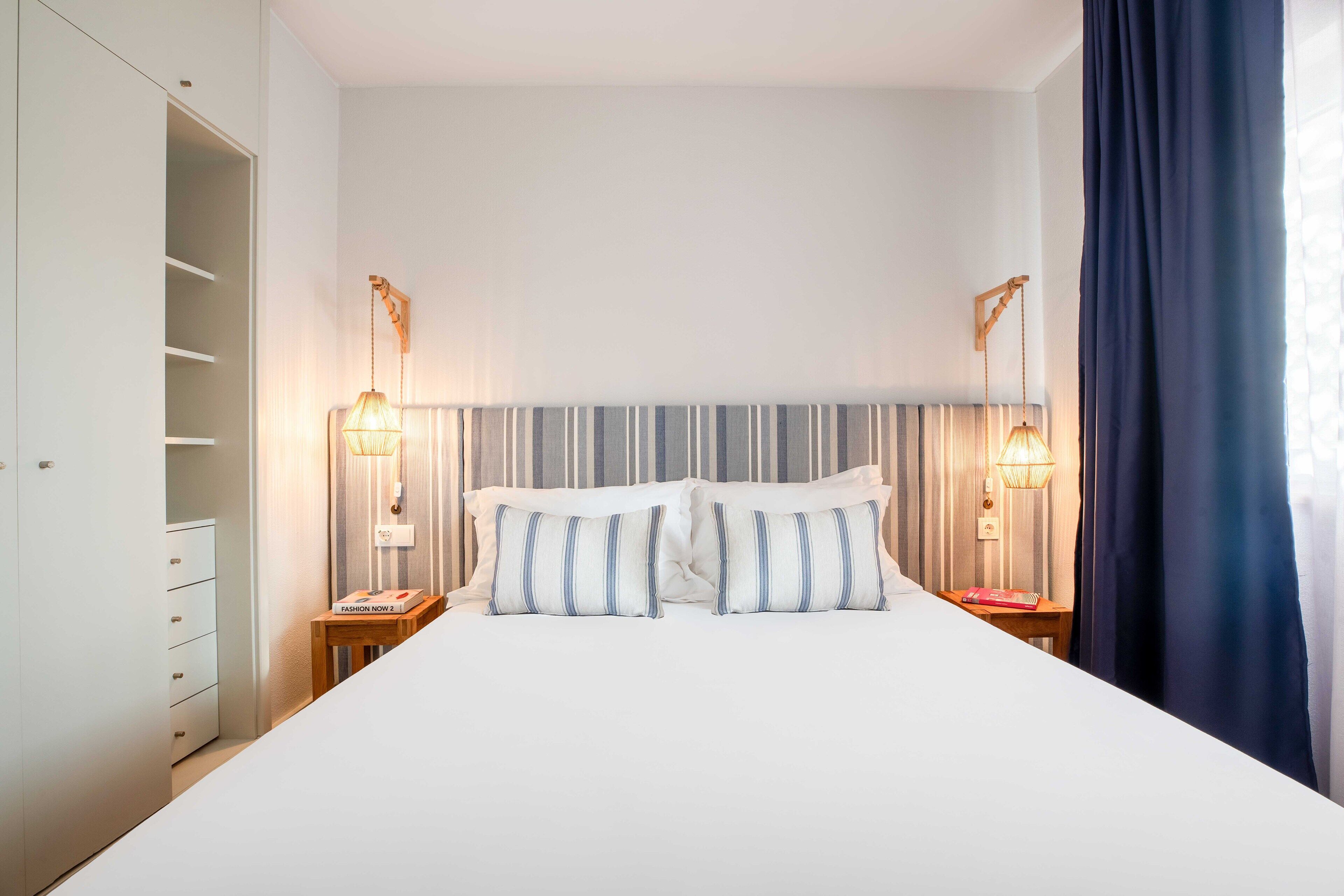A hotel room with a large bed, two bedside tables, a wardrobe, and a window with curtains.