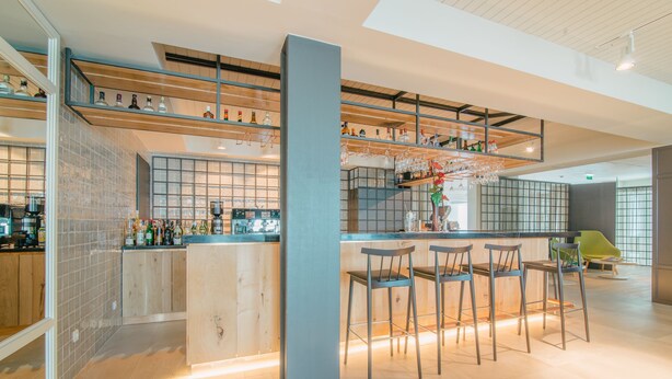 A modern bar area with a wooden counter, bar stools, and a variety of bottles and glasses. - Aqualuz Lagos by The Editory (Lagos)