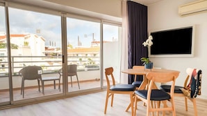 A modern room with a large sliding glass door leading to a balcony, a wooden dining table with chairs, a flat-screen TV mounted on the wall, and a potted orchid on the table. - Aqualuz Lagos by The Editory (Lagos)