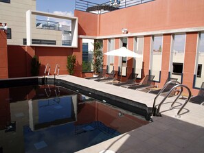 A swimming pool with a sun lounger area, a ladder, and a small plant. - Eco Alcala Suites (Madrid)