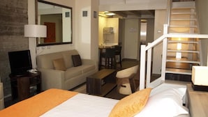 Quarto de hotel com cama, sofá, escrivaninha e escada.