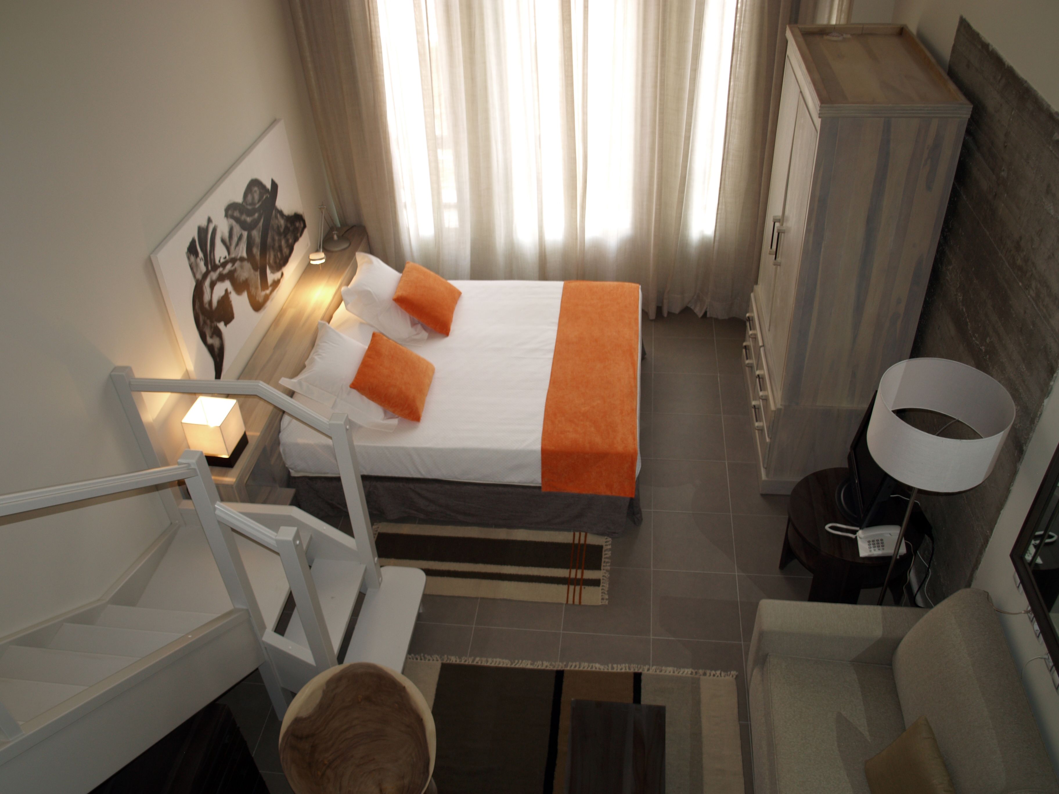 A hotel room with a bed, a desk, a chair, a lamp, and a bathroom area.
