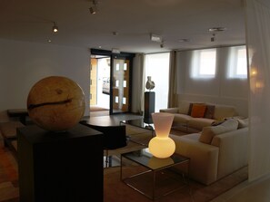 A modern living room with a spherical object on a pedestal, a sofa with cushions, and a table with a lamp. - Eco Alcala Suites (Madrid)