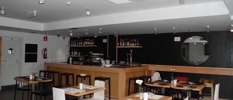 Un restaurante con varias mesas y sillas, una zona de bar con estantes llenos de botellas y un extintor en la pared.
